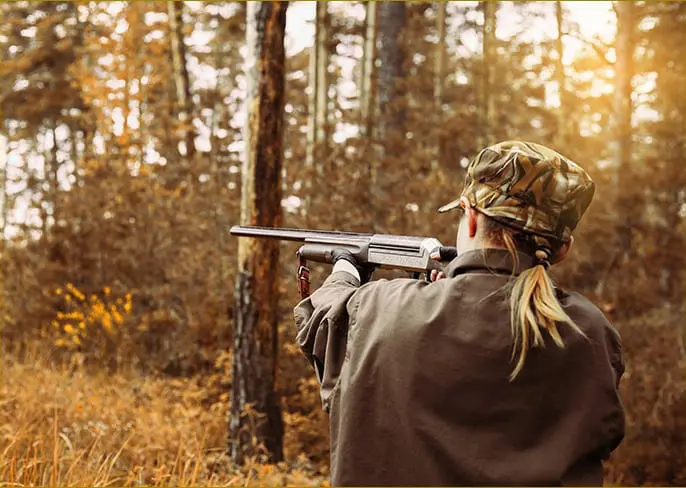 A woman hunting in sunny woods, using hearing plugs