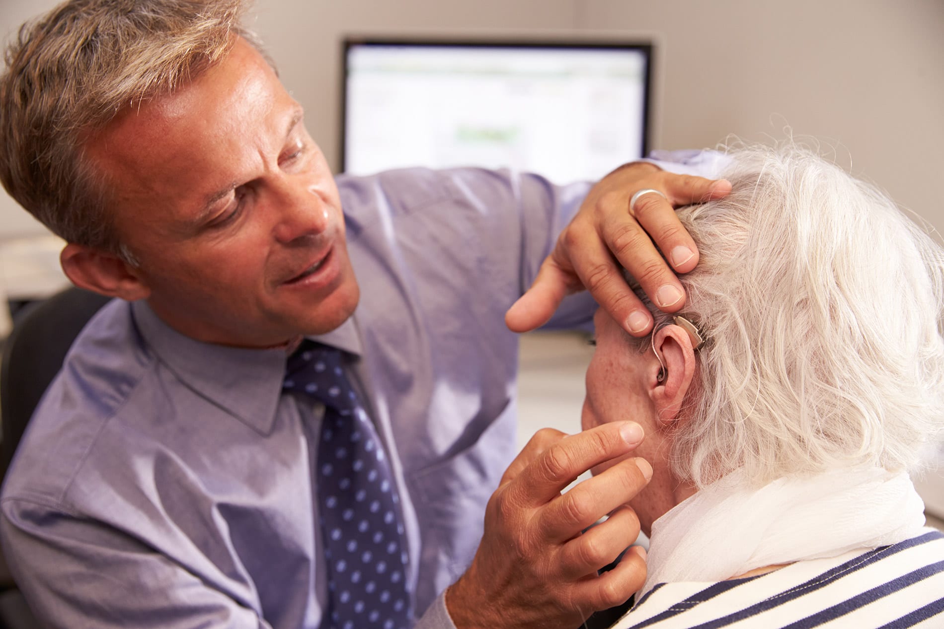 A professional helping a patient test a hearing device